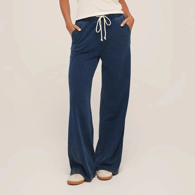 Woman wearing a white top and blue drawstring pants on a plain background