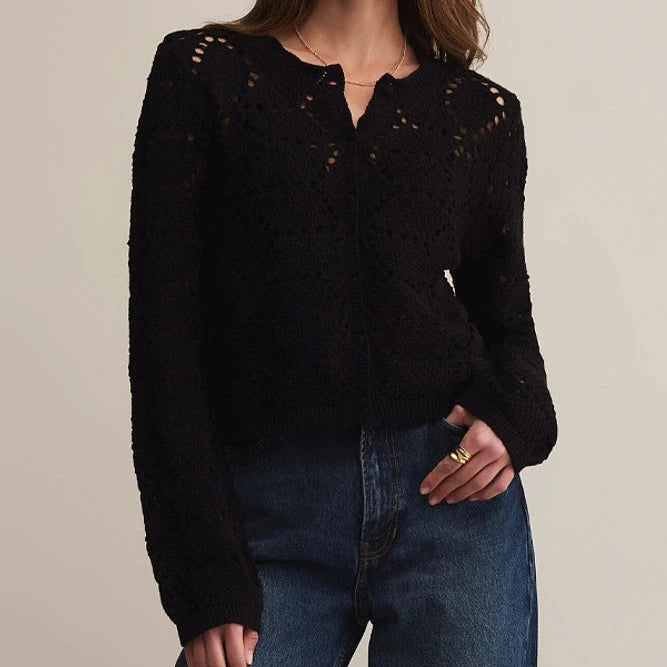 Woman wearing a black knit cardigan and blue jeans against a beige background