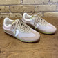 White sneakers with beige accents on a wooden surface with a brick wall background