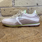 Sneaker with a mix of beige, white, and green colors on a wooden surface with a brick wall background.