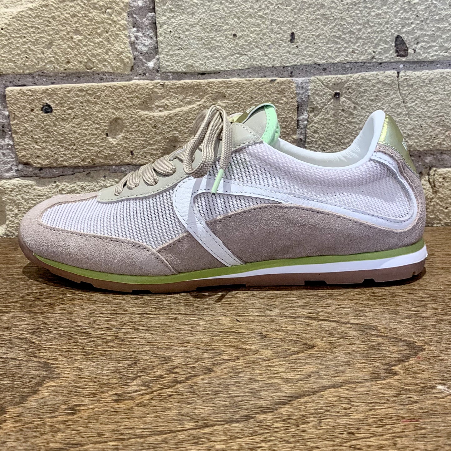 Sneaker with a mix of beige, white, and green colors on a wooden surface with a brick wall background.