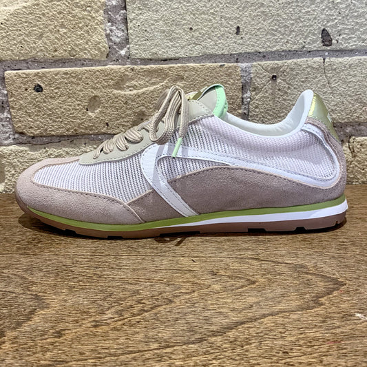 Sneaker with a mix of beige, white, and green colors on a wooden surface with a brick wall background.