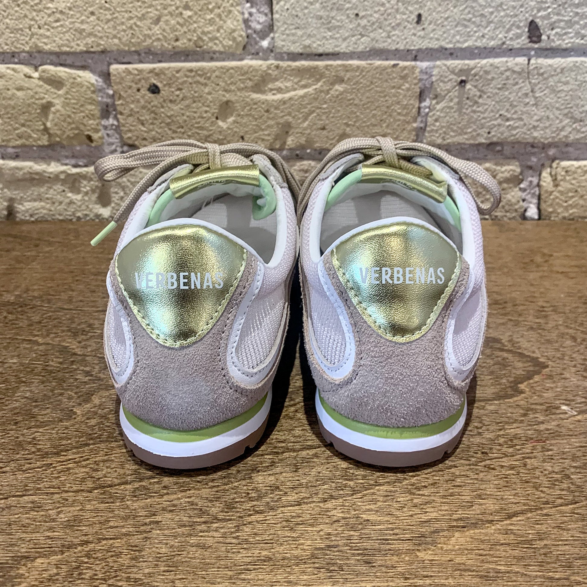 Pair of 'VERBENAS' sneakers on a wooden surface with a brick wall background