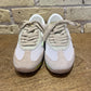 Pair of beige and white sneakers on a wooden surface with a stone wall background