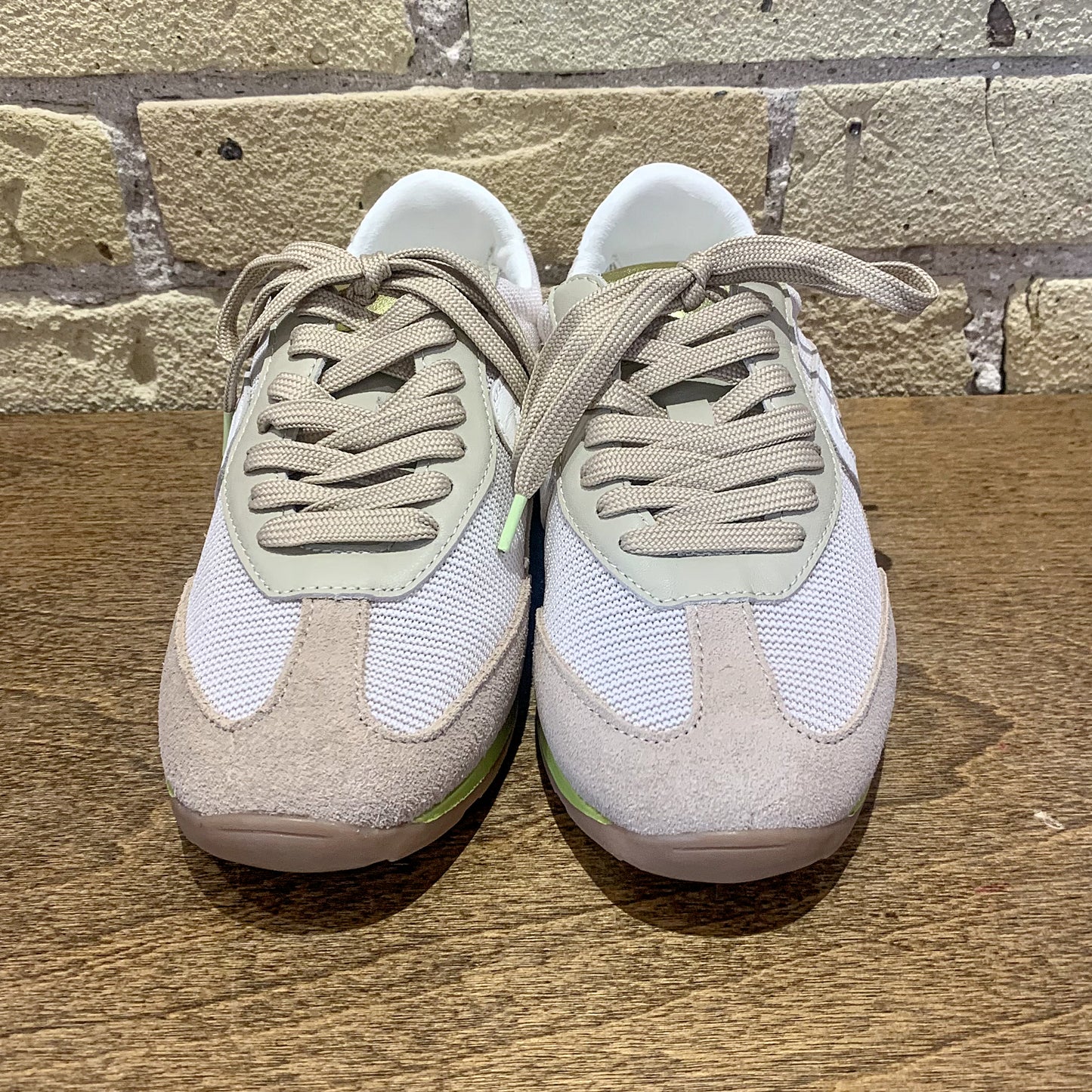 Pair of beige and white sneakers on a wooden surface with a stone wall background
